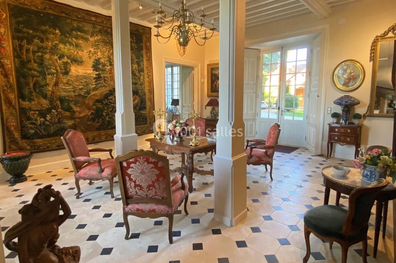 Salon élégant avec tapisseries murales, mobilier ancien, lustre et sol en carreaux noirs et blancs.