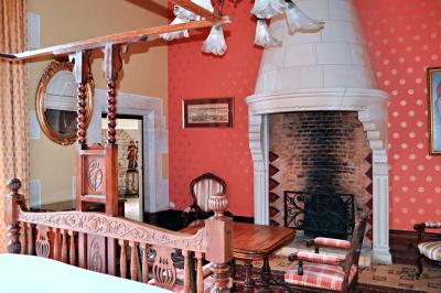 Vase de pivoines roses sur une table en bois, entouré de livres, chandeliers et fauteuils dans un salon élégant.