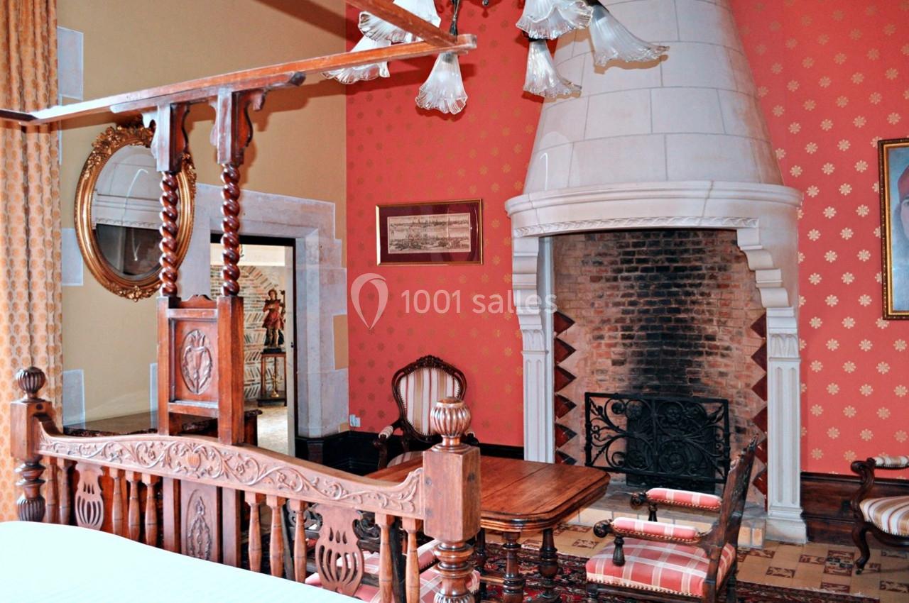 Chambre avec lit en bois sculpté, cheminée en pierre, murs rouges décorés et mobilier ancien.