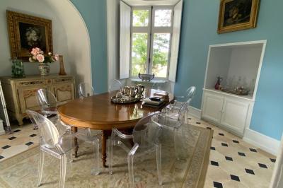 Vase de pivoines roses sur une table en bois, entouré de livres, chandeliers et fauteuils dans un salon élégant.