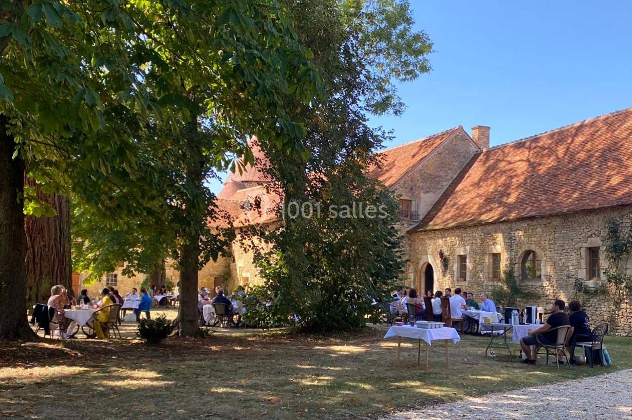Personnes assises à des tables en plein air devant un bâtiment en pierre sous un ciel dégagé.