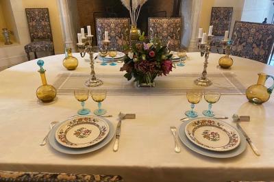 Vase de pivoines roses sur une table en bois, entouré de livres, chandeliers et fauteuils dans un salon élégant.