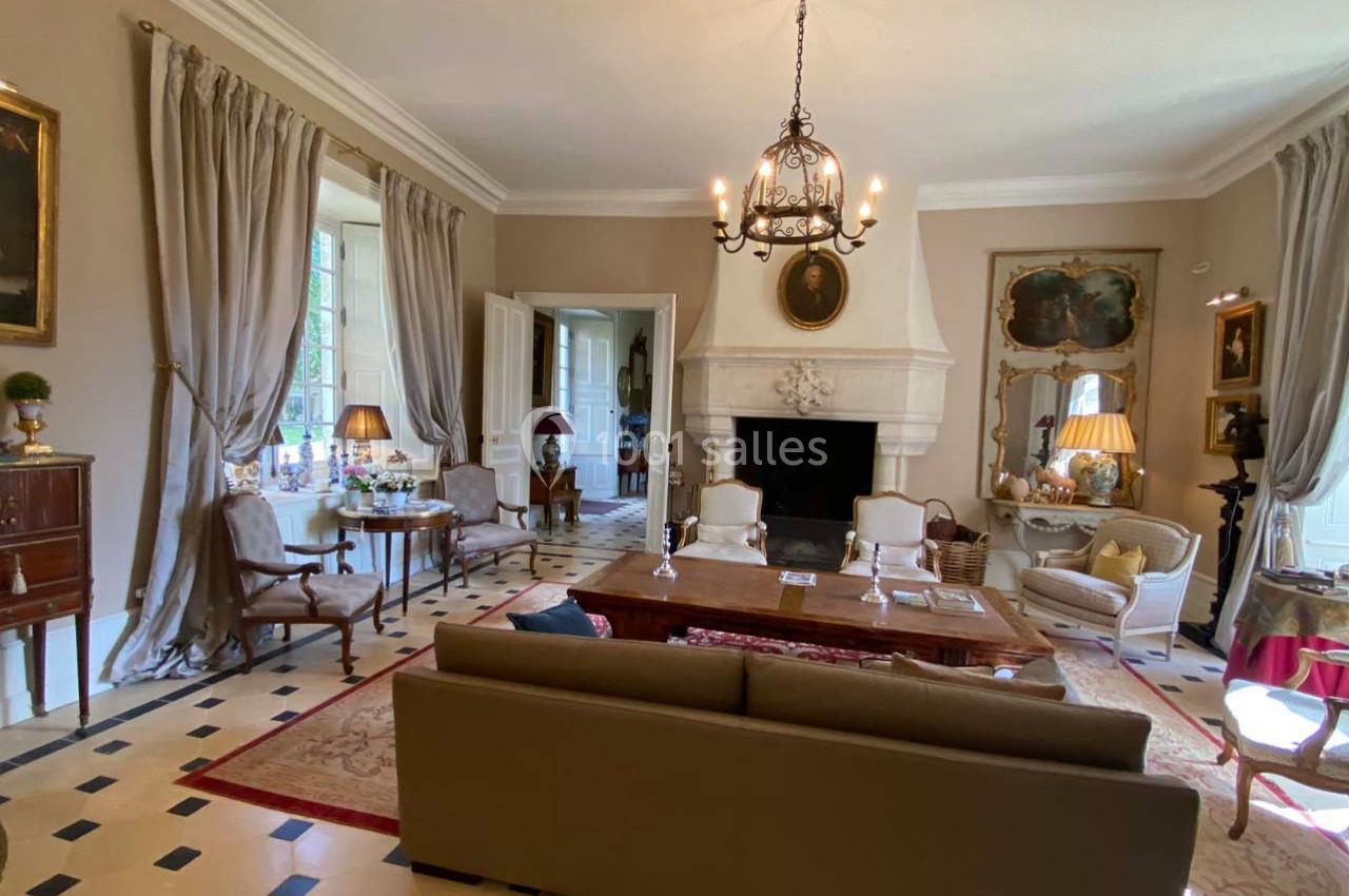 Salon élégant avec cheminée, mobilier classique, lustre en fer forgé, grandes fenêtres et rideaux beiges.