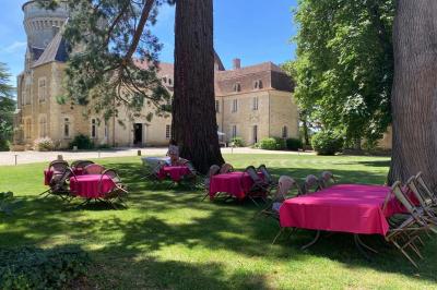 Bâtiment en pierre avec toit en tuiles rouges, entouré d'arbres et d'une pelouse, sous un ciel partiellement nuageux.