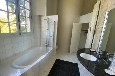 Bâtiment en pierre avec toit en tuiles rouges, entouré d'arbres et d'une pelouse, sous un ciel partiellement nuageux.