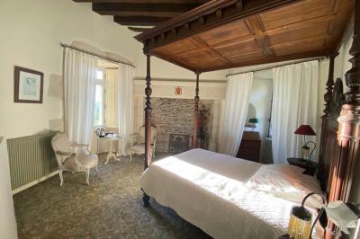 Bâtiment en pierre avec toit en tuiles rouges, entouré d'arbres et d'une pelouse, sous un ciel partiellement nuageux.