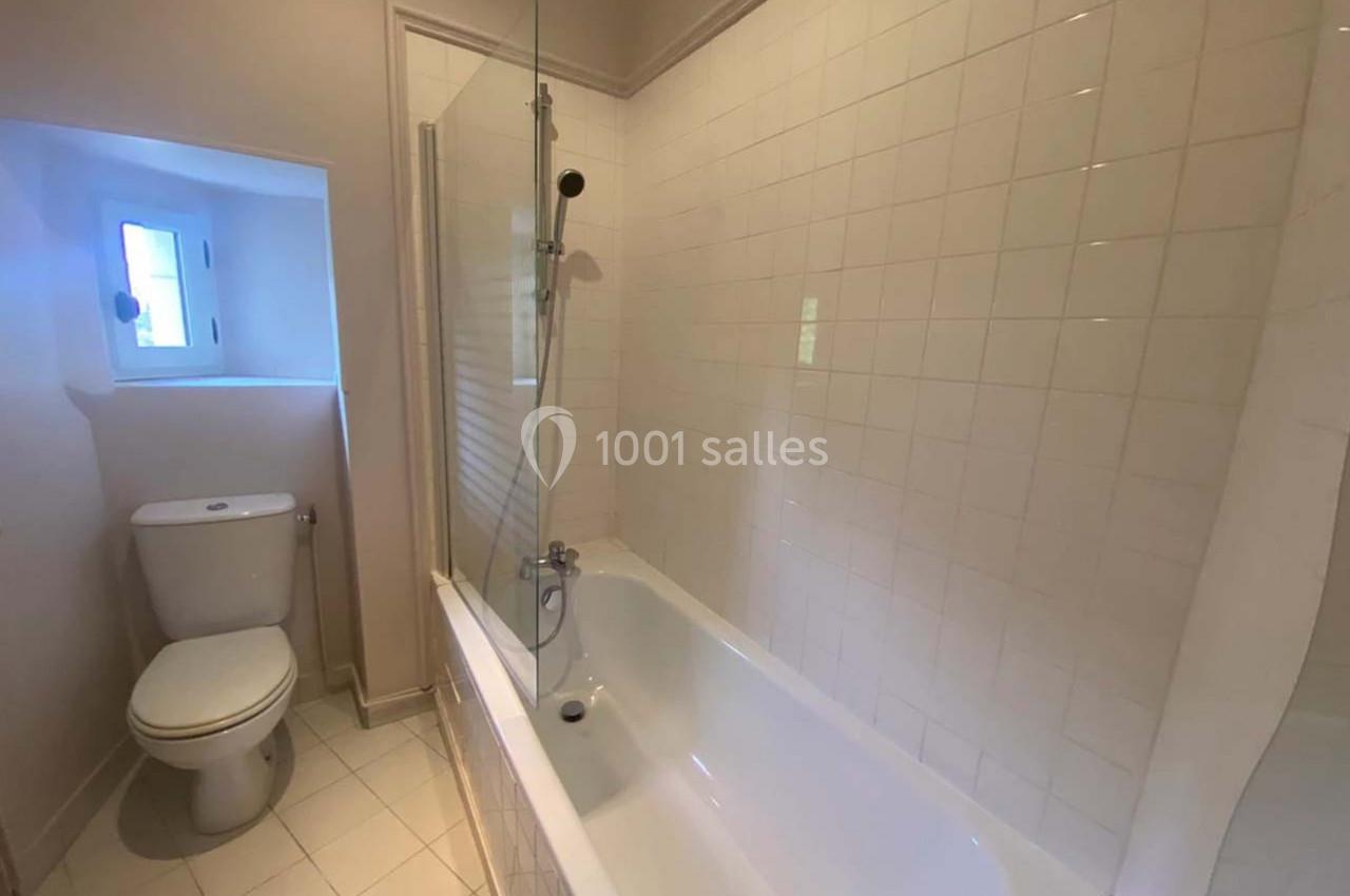 Salle de bain avec baignoire, paroi vitrée, carrelage blanc et petite fenêtre laissant entrer la lumière naturelle.