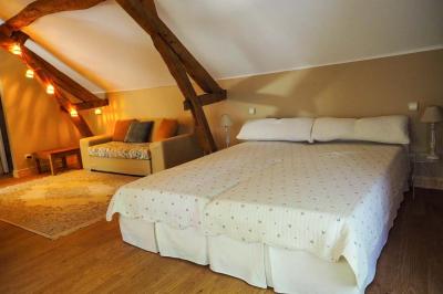 Bâtiment en pierre avec toit en tuiles rouges, entouré d'arbres et d'une pelouse, sous un ciel partiellement nuageux.