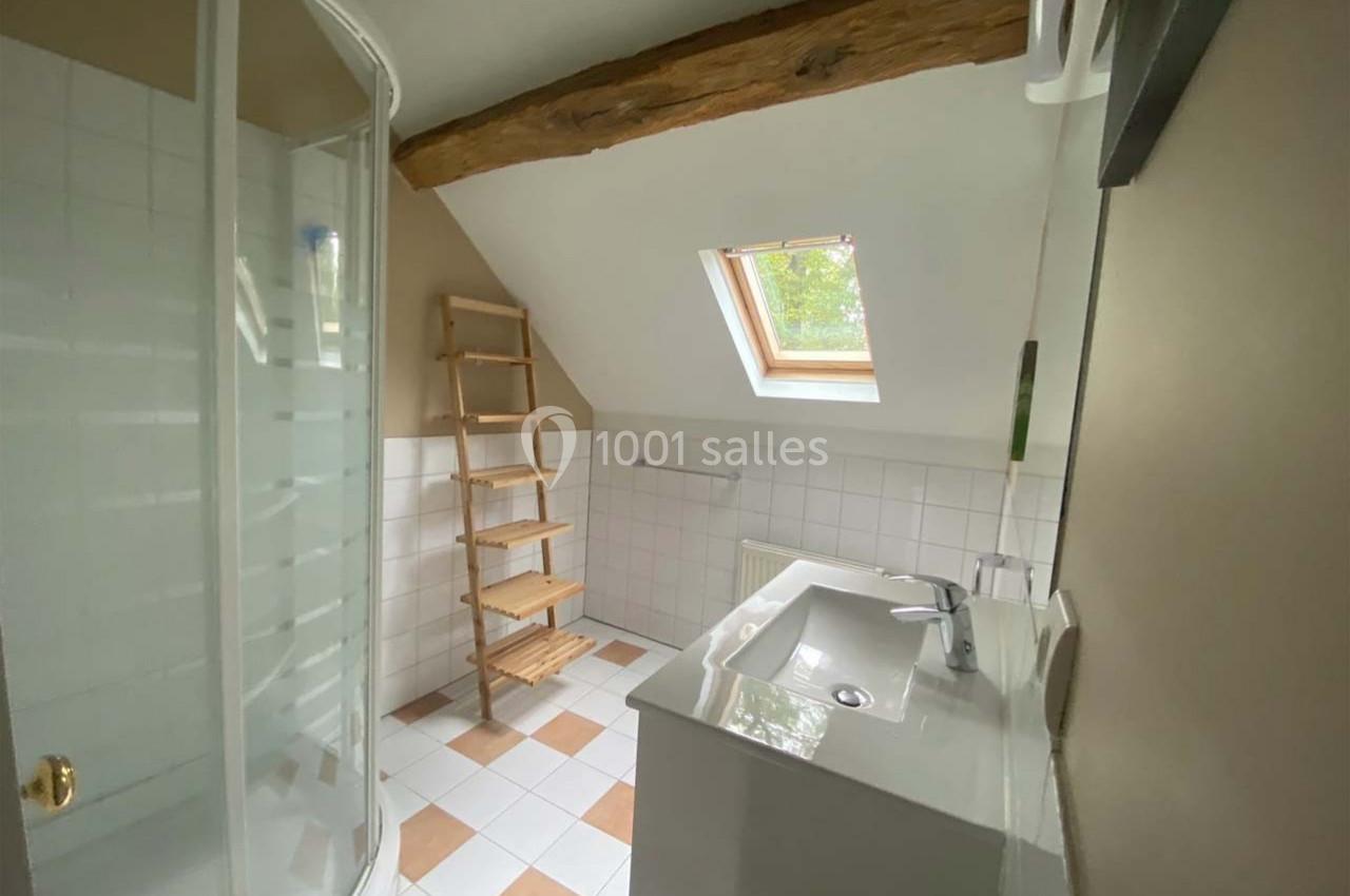 Salle de bain lumineuse avec douche d'angle, lavabo moderne, étagère en bois et fenêtre de toit.