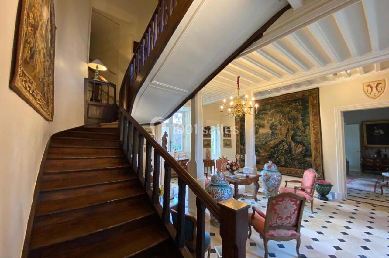 Escalier en bois menant à l'étage dans un intérieur élégant avec tapisseries, meubles anciens et sol en damier.