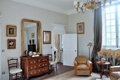 Bâtiment en pierre avec toit en tuiles rouges, entouré d'arbres et d'une pelouse, sous un ciel partiellement nuageux.