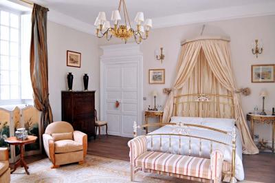 Bâtiment en pierre avec toit en tuiles rouges, entouré d'arbres et d'une pelouse, sous un ciel partiellement nuageux.