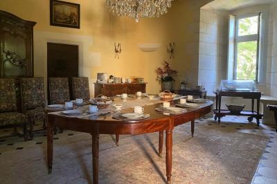 Bâtiment en pierre avec toit en tuiles rouges, entouré d'arbres et d'une pelouse, sous un ciel partiellement nuageux.