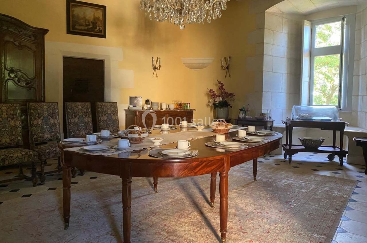 Salle à manger lumineuse avec une table dressée pour le petit-déjeuner, entourée de chaises et décorée d'un lustre.