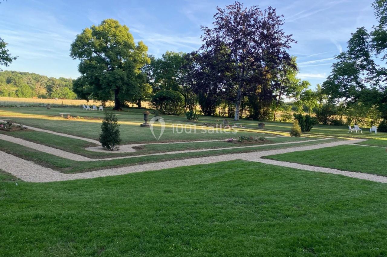 Jardin avec pelouses, allées gravillonnées et arbres, sous un ciel dégagé en fin de journée.