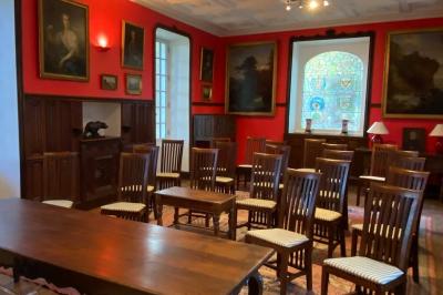 Bâtiment en pierre avec toit en tuiles rouges, entouré d'arbres et d'une pelouse, sous un ciel partiellement nuageux.