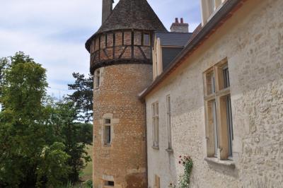 Bâtiment en pierre avec toit en tuiles rouges, entouré d'arbres et d'une pelouse, sous un ciel partiellement nuageux.