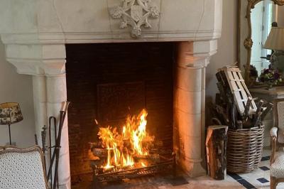 Bâtiment en pierre avec toit en tuiles rouges, entouré d'arbres et d'une pelouse, sous un ciel partiellement nuageux.