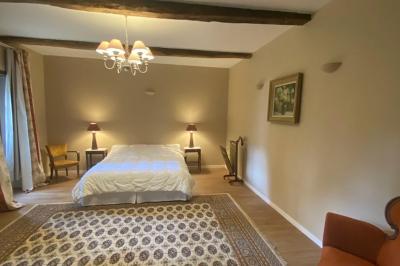 Bâtiment en pierre avec toit en tuiles rouges, entouré d'arbres et d'une pelouse, sous un ciel partiellement nuageux.