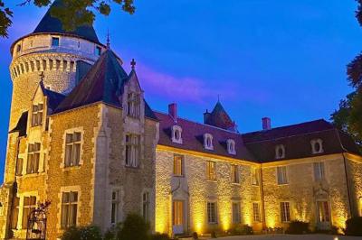 Bâtiment en pierre avec toit en tuiles rouges, entouré d'arbres et d'une pelouse, sous un ciel partiellement nuageux.