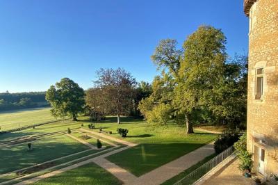 Bâtiment en pierre avec toit en tuiles rouges, entouré d'arbres et d'une pelouse, sous un ciel partiellement nuageux.