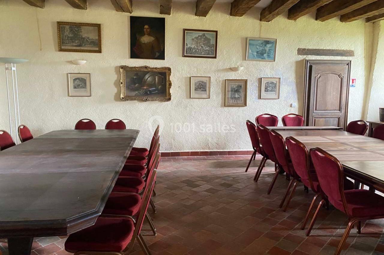 Salle avec des tables en bois, chaises rouges et murs décorés de tableaux et gravures, sous un plafond à poutres apparentes.