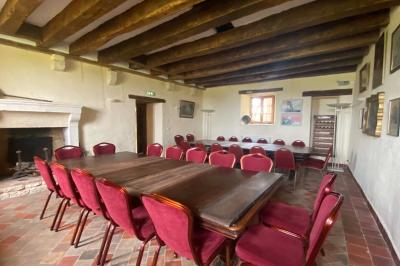 Bâtiment en pierre avec toit en tuiles rouges, entouré d'arbres et d'une pelouse, sous un ciel partiellement nuageux.