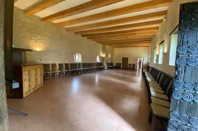 Bâtiment en pierre avec toit en tuiles rouges, entouré d'arbres et d'une pelouse, sous un ciel partiellement nuageux.