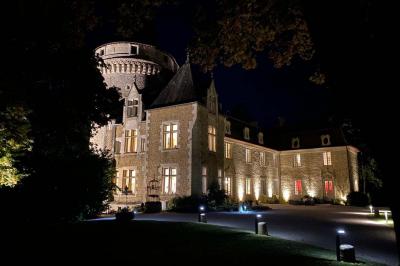 Bâtiment en pierre avec toit en tuiles rouges, entouré d'arbres et d'une pelouse, sous un ciel partiellement nuageux.