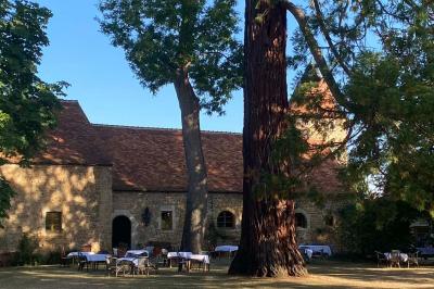 Bâtiment en pierre avec toit en tuiles rouges, entouré d'arbres et d'une pelouse, sous un ciel partiellement nuageux.