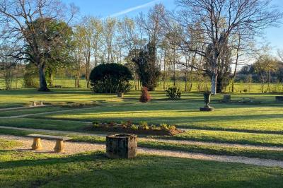 Bâtiment en pierre avec toit en tuiles rouges, entouré d'arbres et d'une pelouse, sous un ciel partiellement nuageux.