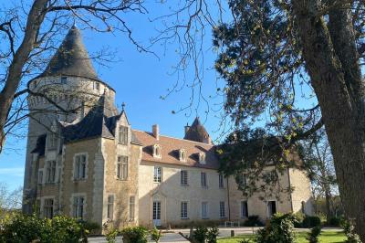 Bâtiment en pierre avec toit en tuiles rouges, entouré d'arbres et d'une pelouse, sous un ciel partiellement nuageux.