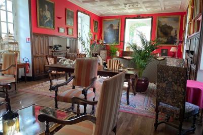 Bâtiment en pierre avec toit en tuiles rouges, entouré d'arbres et d'une pelouse, sous un ciel partiellement nuageux.