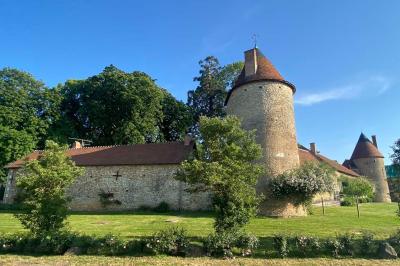 Bâtiment en pierre avec toit en tuiles rouges, entouré d'arbres et d'une pelouse, sous un ciel partiellement nuageux.