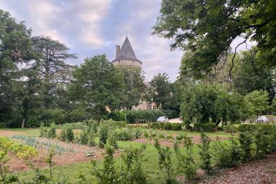 Bâtiment en pierre avec toit en tuiles rouges, entouré d'arbres et d'une pelouse, sous un ciel partiellement nuageux.