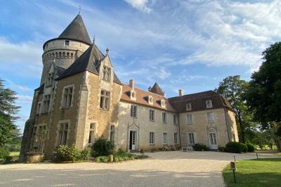 Bâtiment en pierre avec toit en tuiles rouges, entouré d'arbres et d'une pelouse, sous un ciel partiellement nuageux.