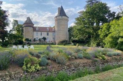 Bâtiment en pierre avec toit en tuiles rouges, entouré d'arbres et d'une pelouse, sous un ciel partiellement nuageux.