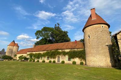 Bâtiment en pierre avec toit en tuiles rouges, entouré d'arbres et d'une pelouse, sous un ciel partiellement nuageux.