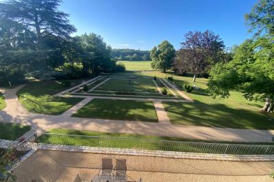 Bâtiment en pierre avec toit en tuiles rouges, entouré d'arbres et d'une pelouse, sous un ciel partiellement nuageux.