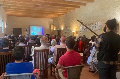 Bâtiment en pierre avec toit en tuiles rouges, entouré d'arbres et d'une pelouse, sous un ciel partiellement nuageux.