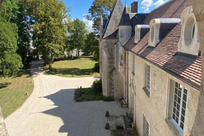Bâtiment en pierre avec toit en tuiles rouges, entouré d'arbres et d'une pelouse, sous un ciel partiellement nuageux.