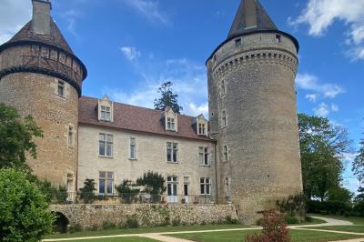 Bâtiment en pierre avec toit en tuiles rouges, entouré d'arbres et d'une pelouse, sous un ciel partiellement nuageux.