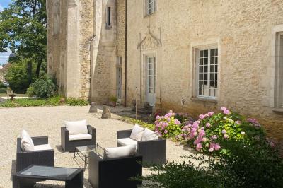 Bâtiment en pierre avec toit en tuiles rouges, entouré d'arbres et d'une pelouse, sous un ciel partiellement nuageux.