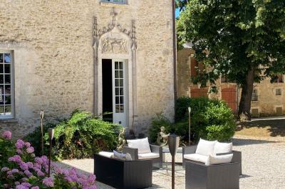 Bâtiment en pierre avec toit en tuiles rouges, entouré d'arbres et d'une pelouse, sous un ciel partiellement nuageux.