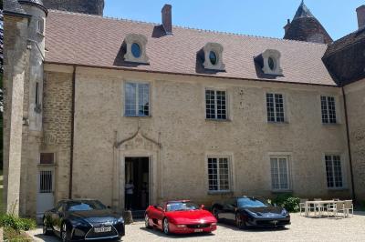 Bâtiment en pierre avec toit en tuiles rouges, entouré d'arbres et d'une pelouse, sous un ciel partiellement nuageux.