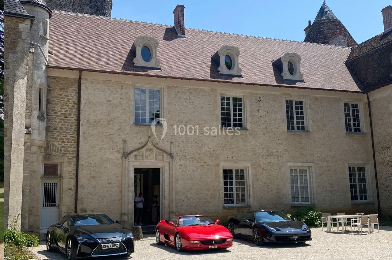 Façade d'un bâtiment ancien en pierre avec trois voitures de sport garées devant sur une cour pavée.