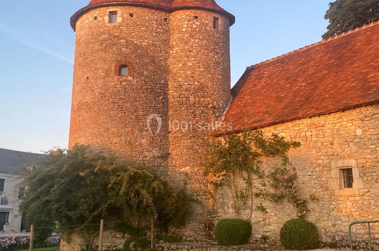 Tour en pierre ancienne avec toit en tuiles rouges, éclairée par une lumière chaude au coucher du soleil.