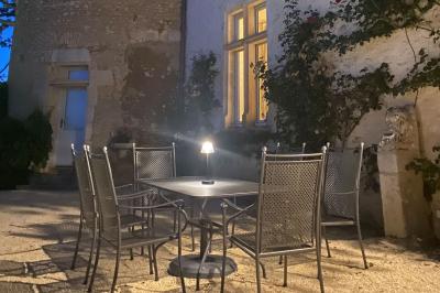 Bâtiment en pierre avec toit en tuiles rouges, entouré d'arbres et d'une pelouse, sous un ciel partiellement nuageux.