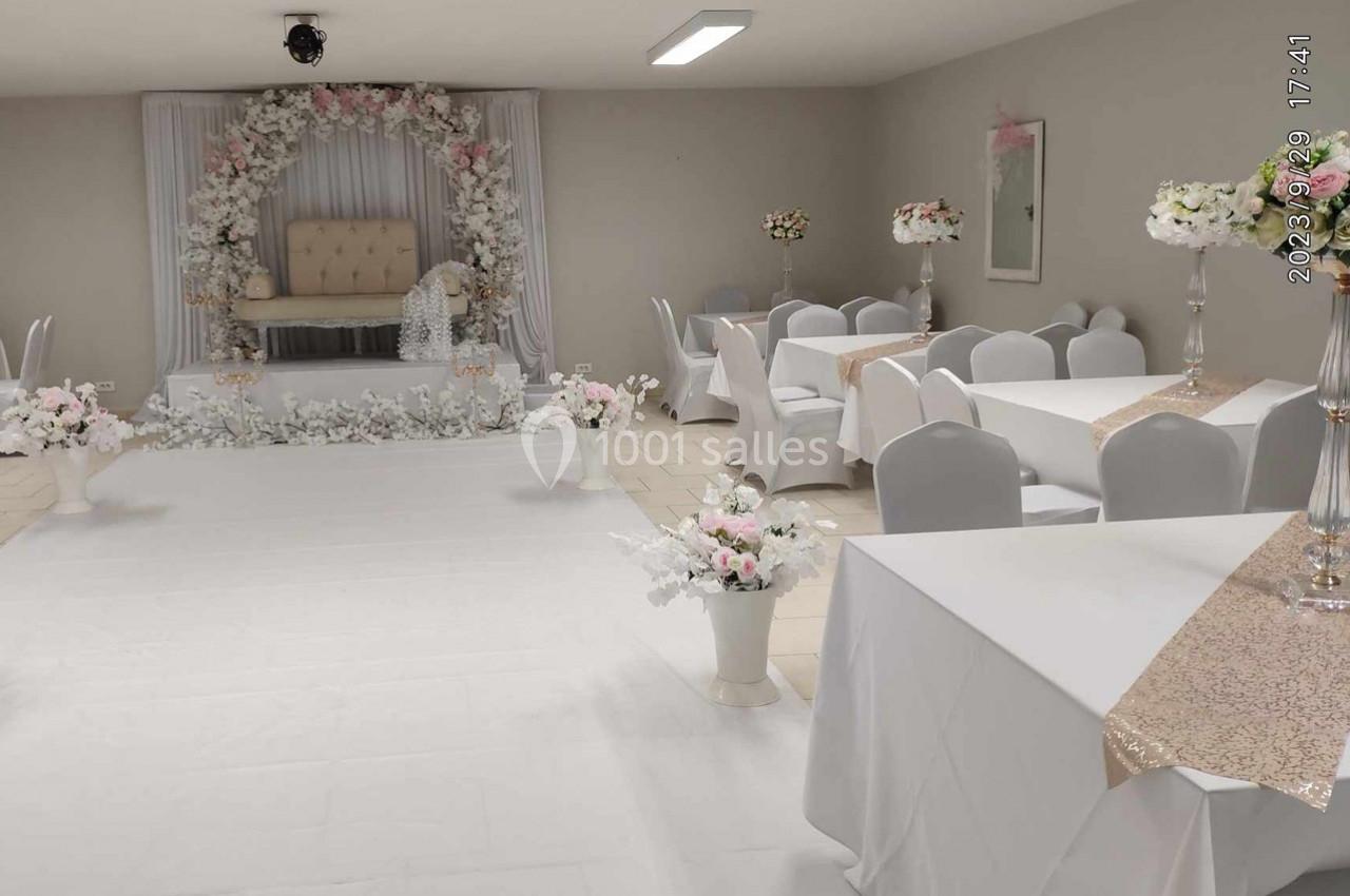 Salle décorée pour un événement avec arche florale, chaises blanches, nappes et arrangements floraux élégants.