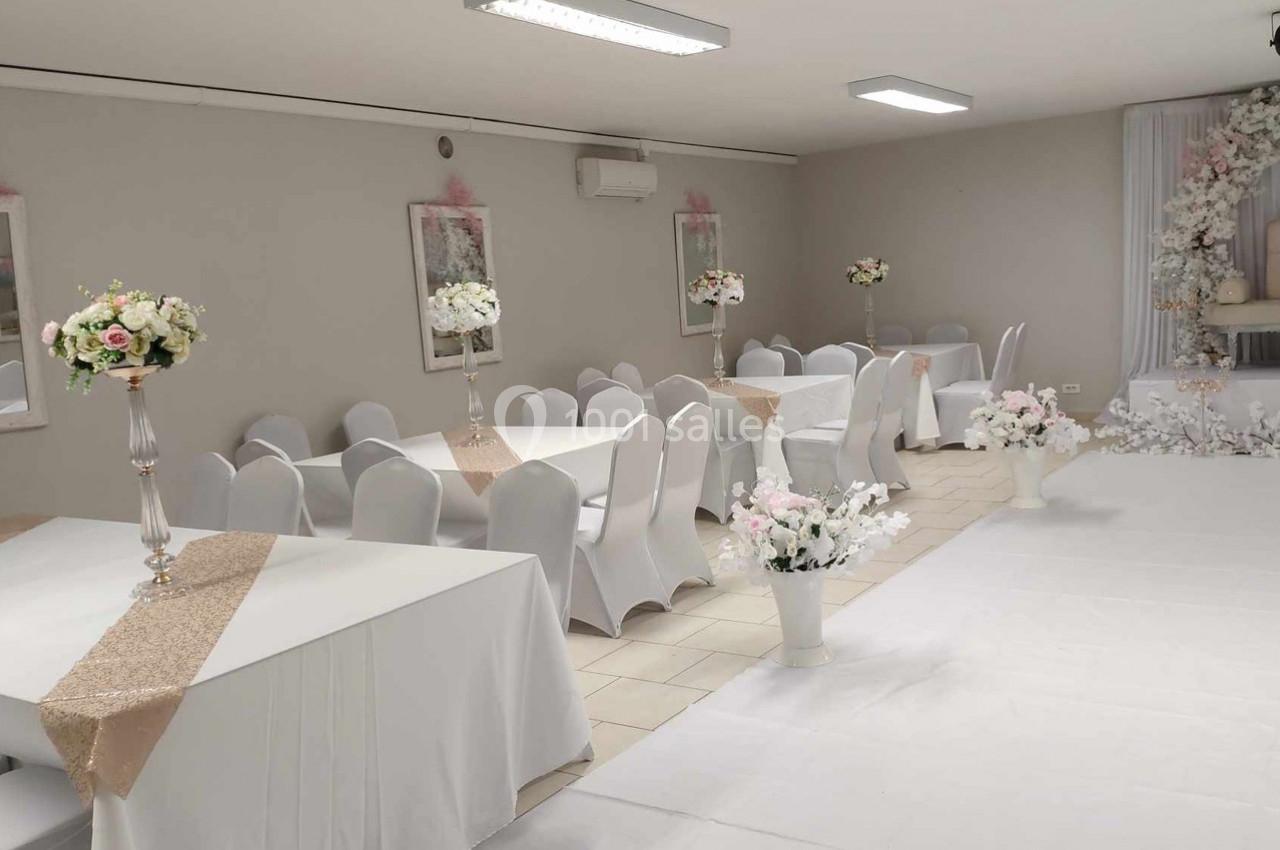 Salle de réception décorée avec des tables blanches, nappes dorées, chaises houssées et arrangements floraux élégants.